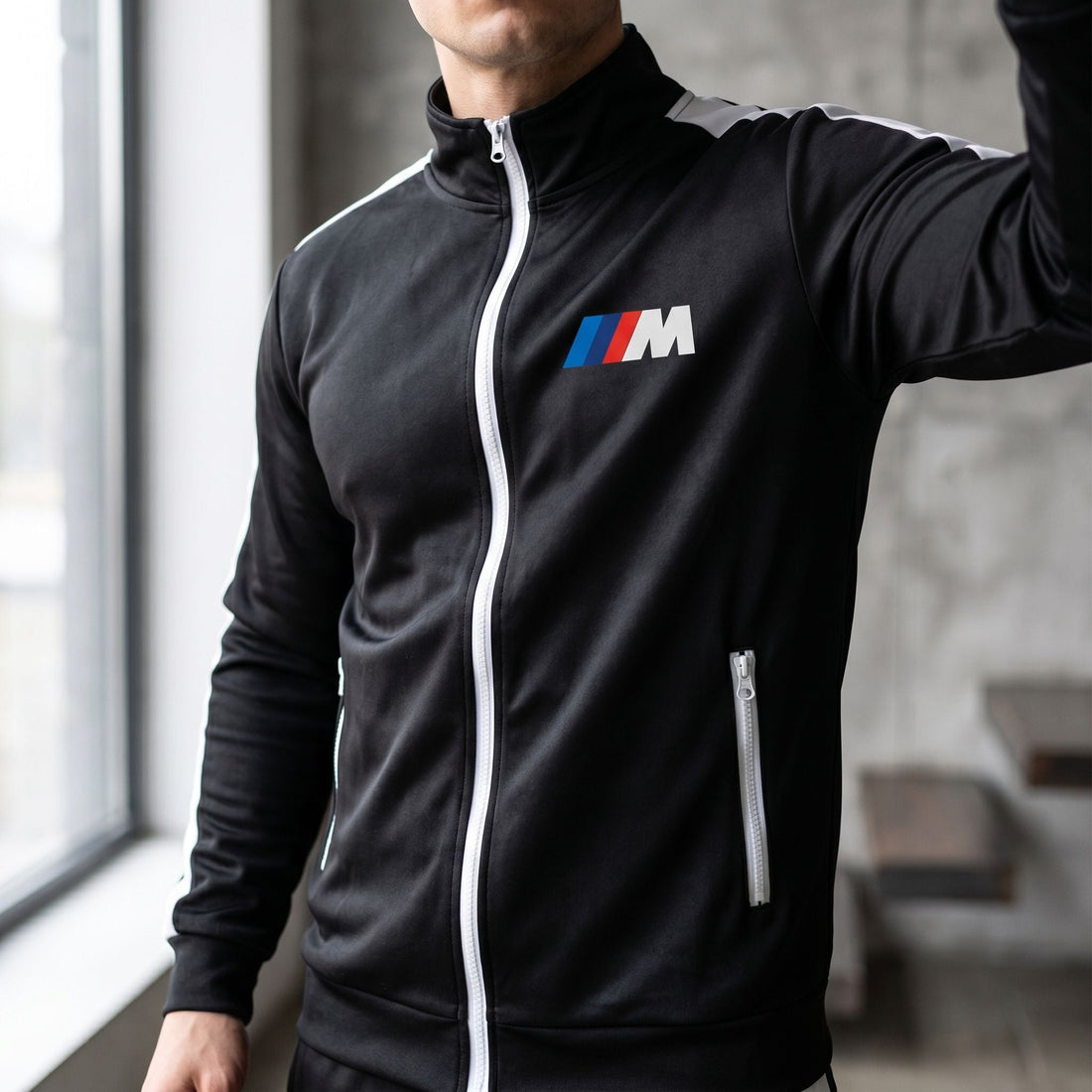 Close-up of male model's upper torso wearing BMW M Dri-Fit Track Suit in natural light, showcasing fit and material sheen in interior setting.