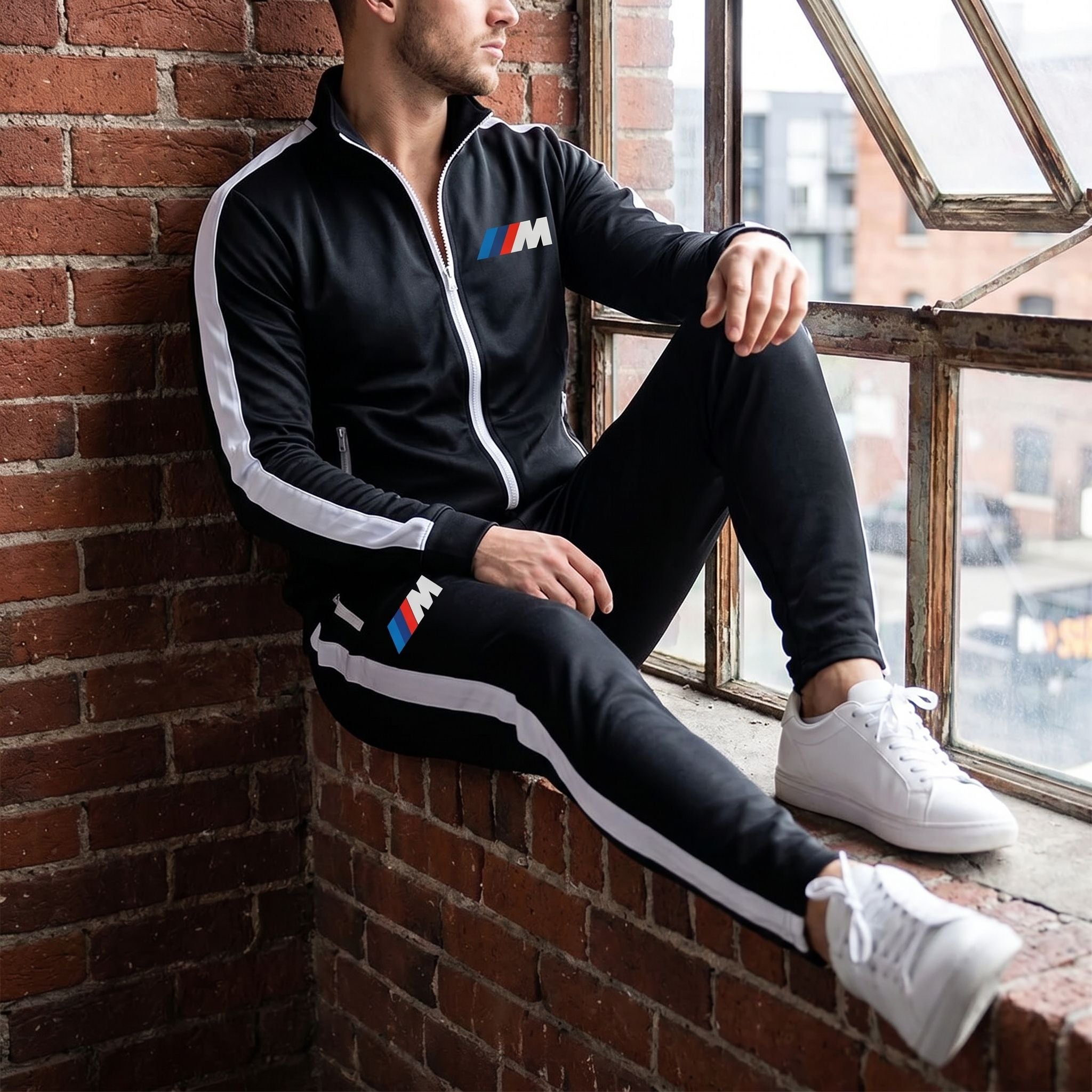 Casual scene of male model relaxing against brick wall in BMW M Dri-Fit Track Suit, highlighting relaxed fit and fabric details in natural light.